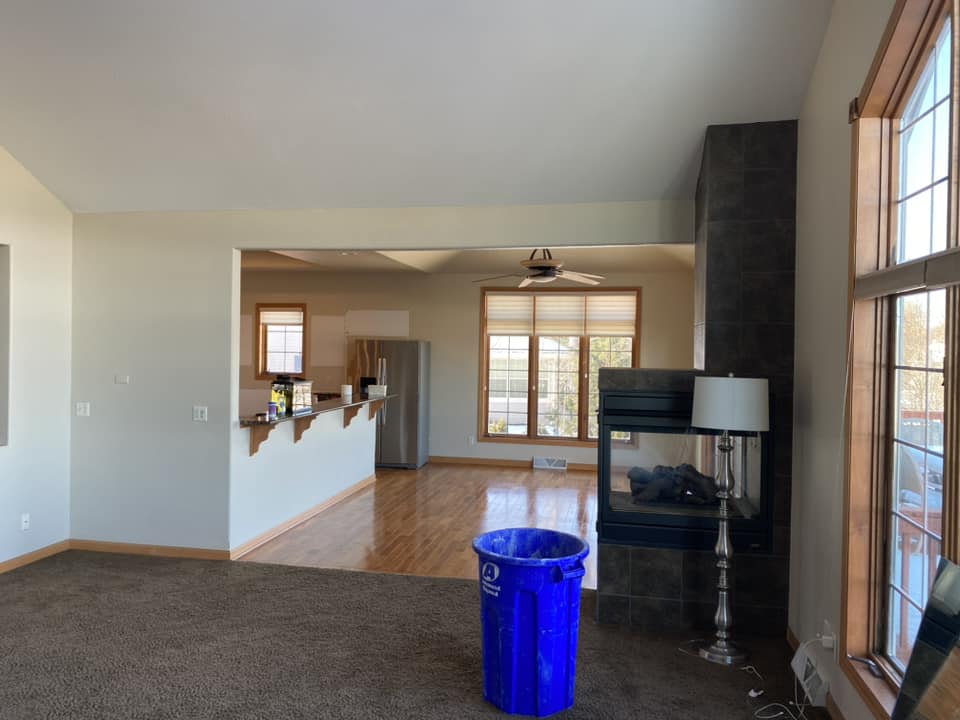 Existing open-plan living and dining area before renovation with two-sided tile fireplace and hardwood floors